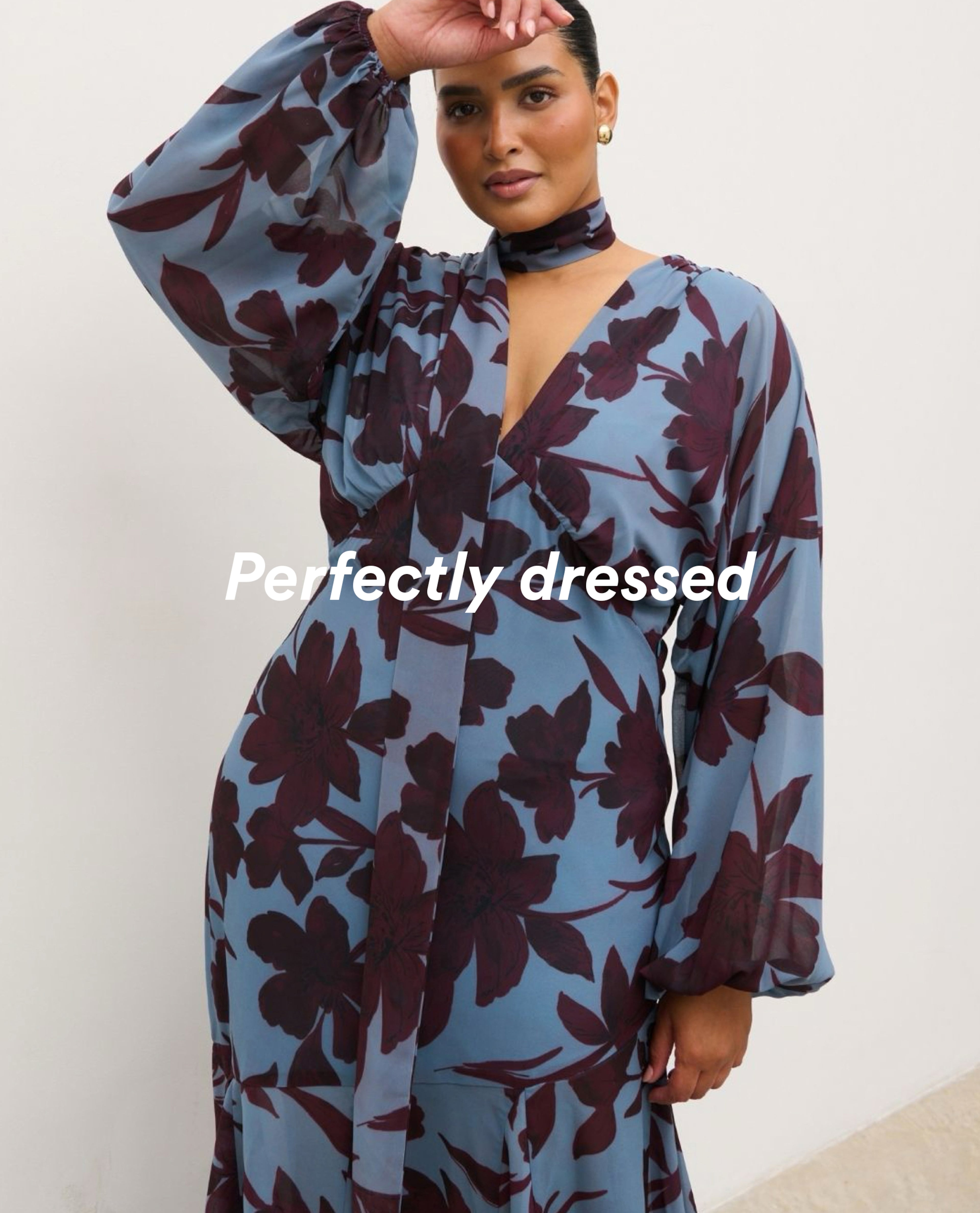 Woman wearing a blue floral dress with a matching neck scarf and long sleeves.