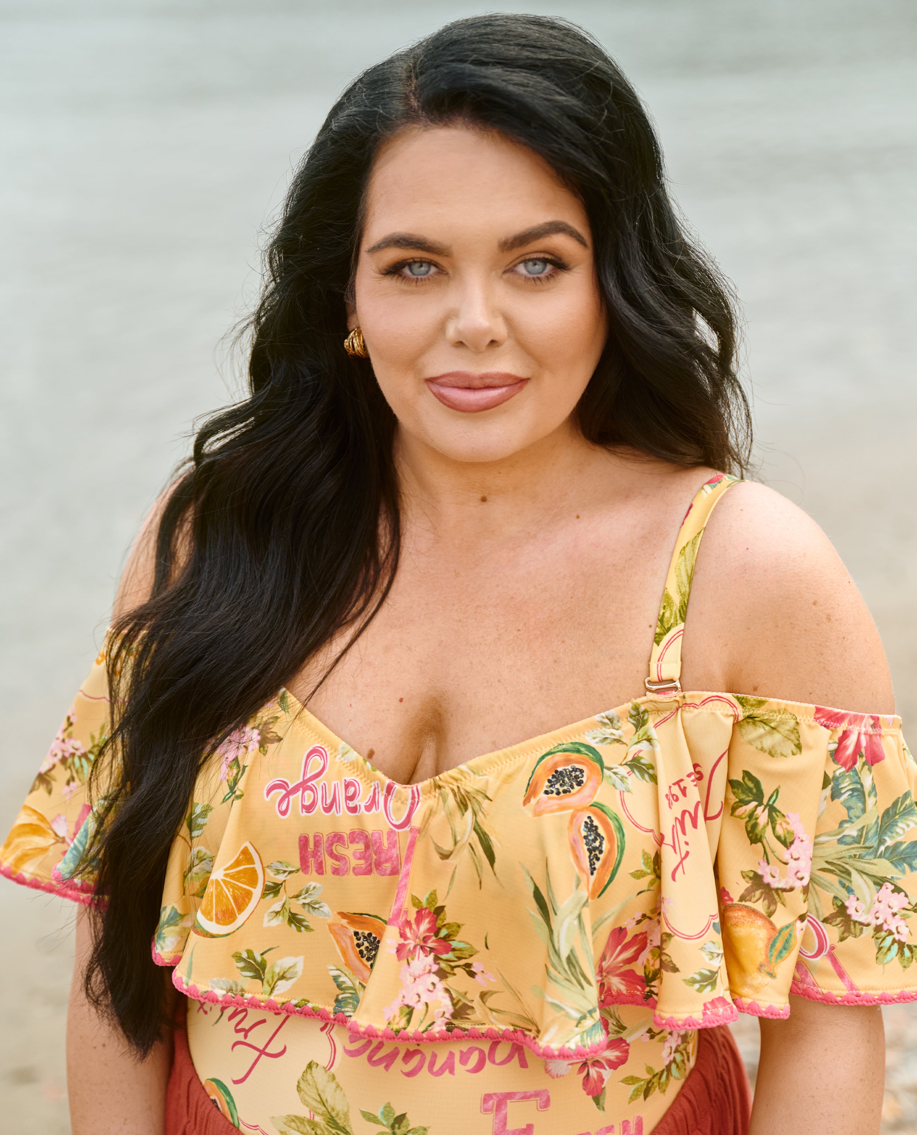 Close-up portrait of a person in a yellow off-shoulder floral top with gold earrings