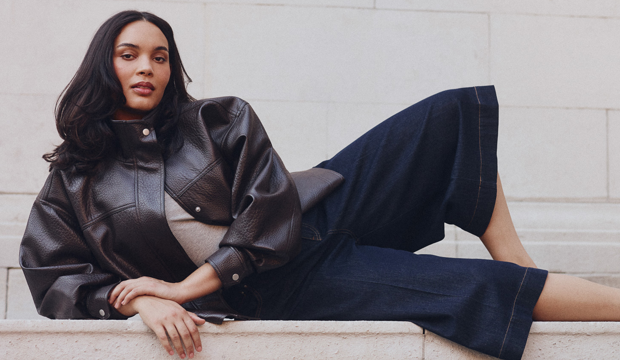 Model is wearing a brown leather jacket with dark denim cropped trousers.
