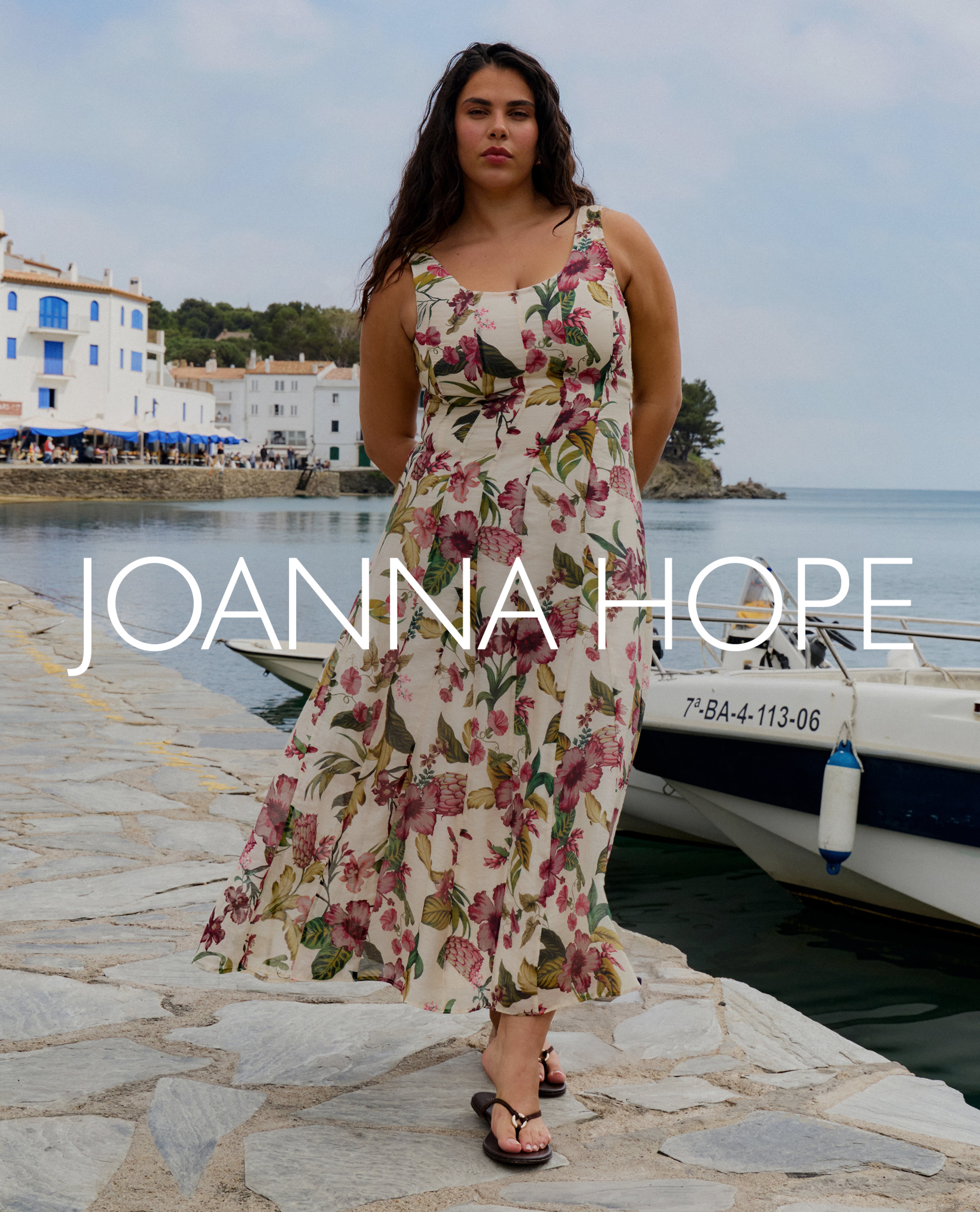 Person in a floral sleeveless midi dress walking along a seaside harbour, text reads ‘Joanna Hope’