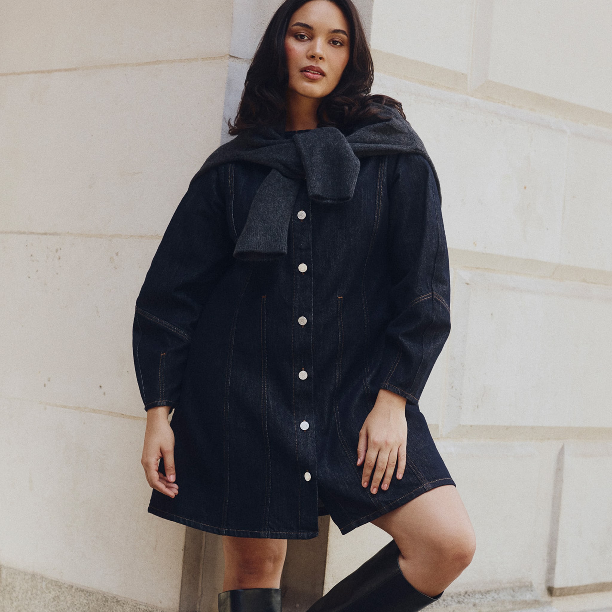 Model is wearing an indigo denim button front mini dress with a pair of black boots.