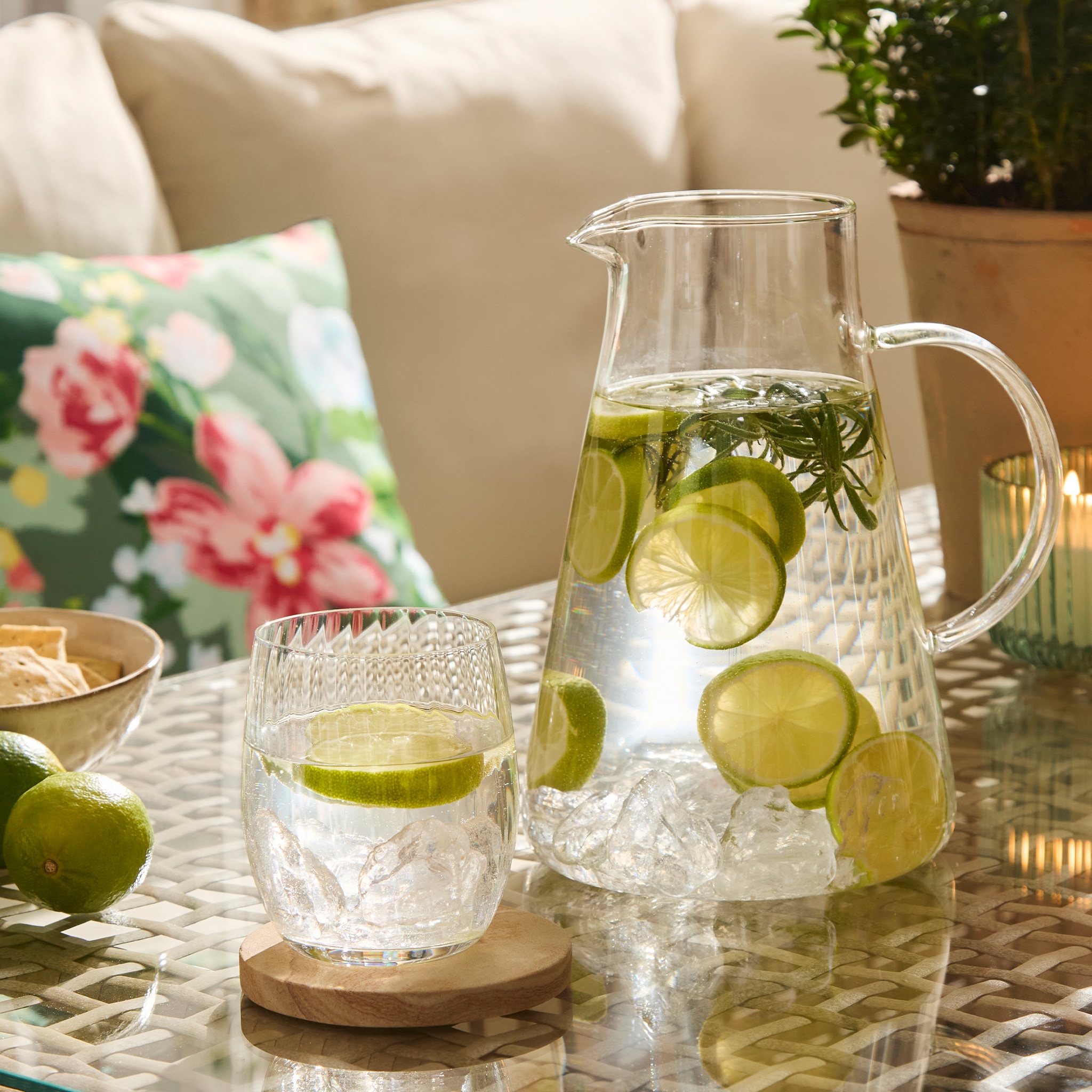 Jug and glass filled with water and lime. Sitting on table.