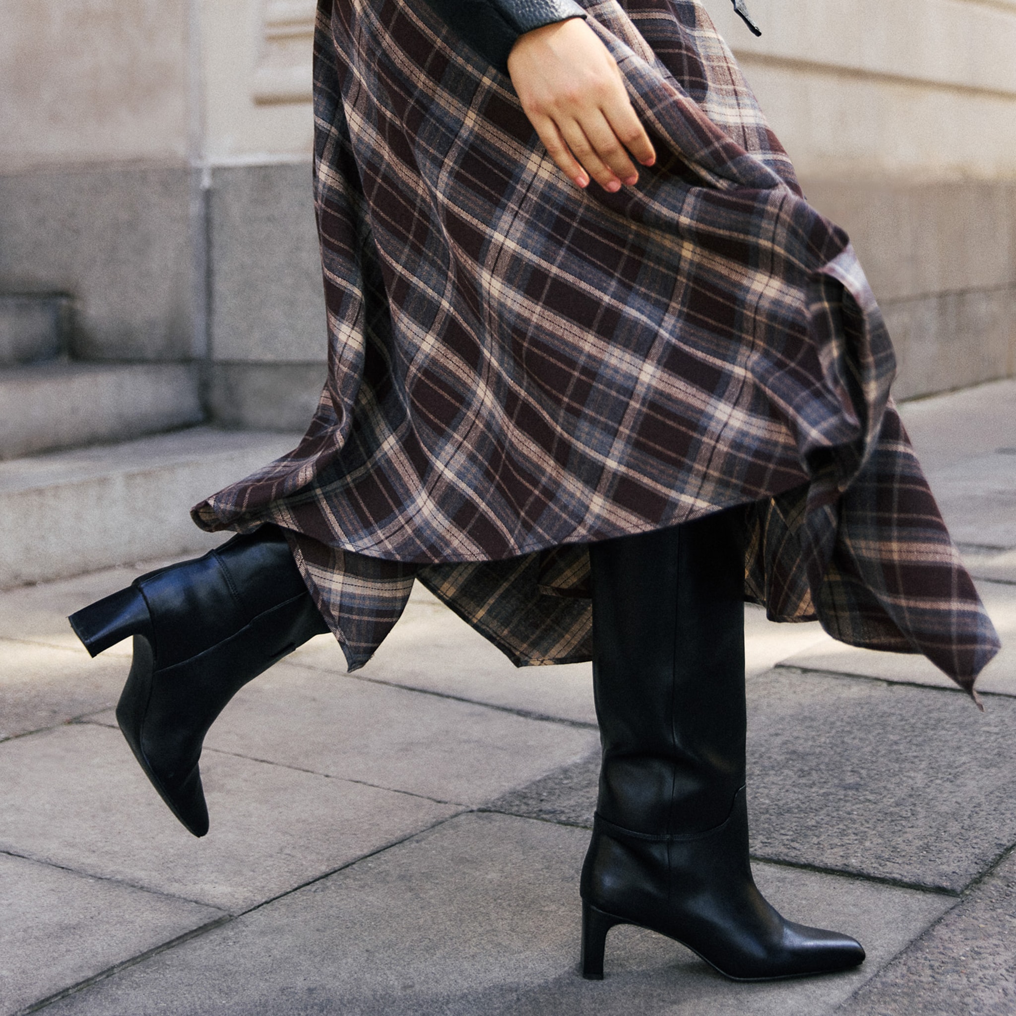 Model is wearing a tartan skirts with a pair of black heeled boots.