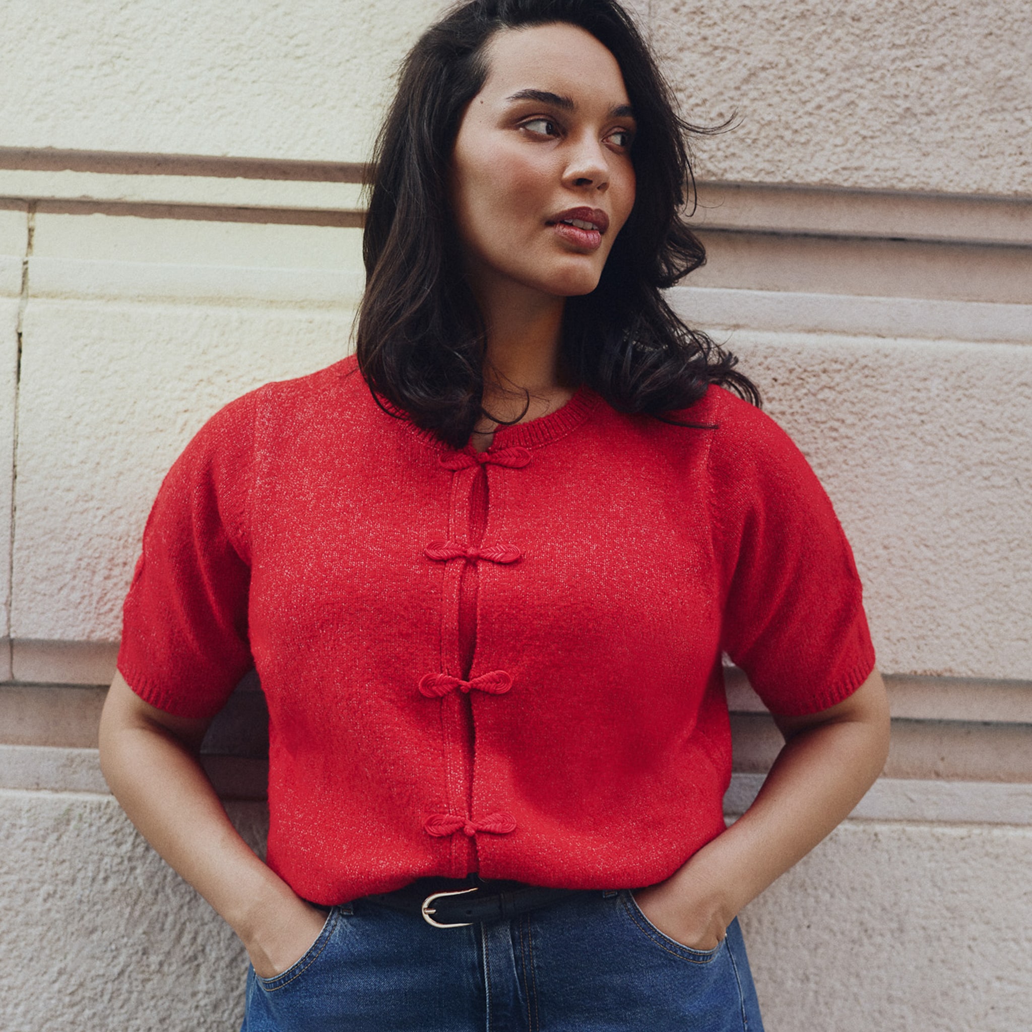 Model is wearing a red knitted  cardigan with denim jeans.