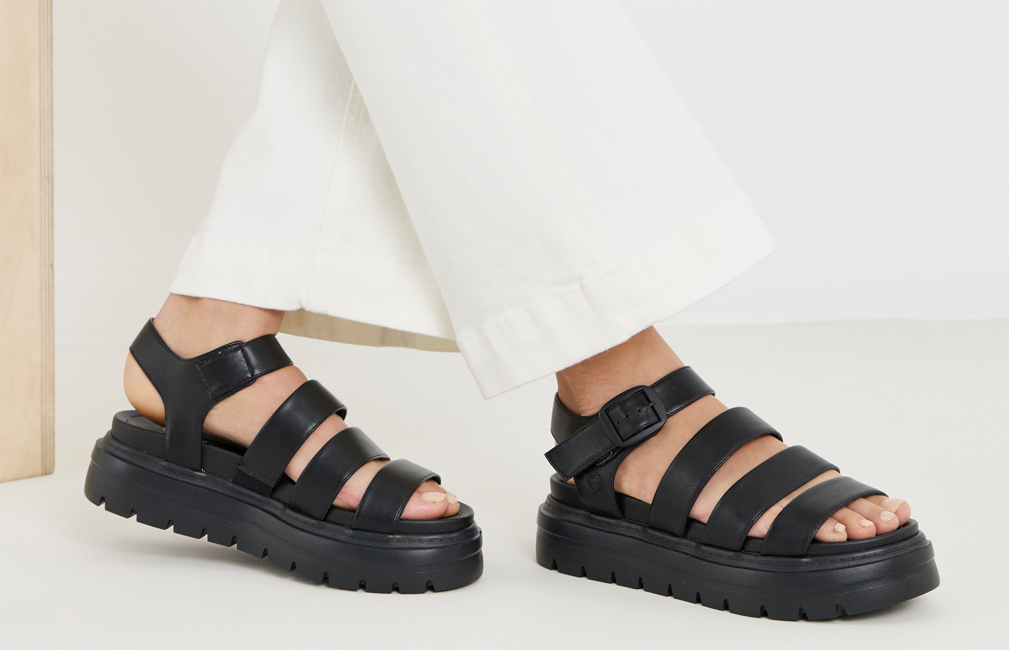 Model wearing cream pants black strap sandals
