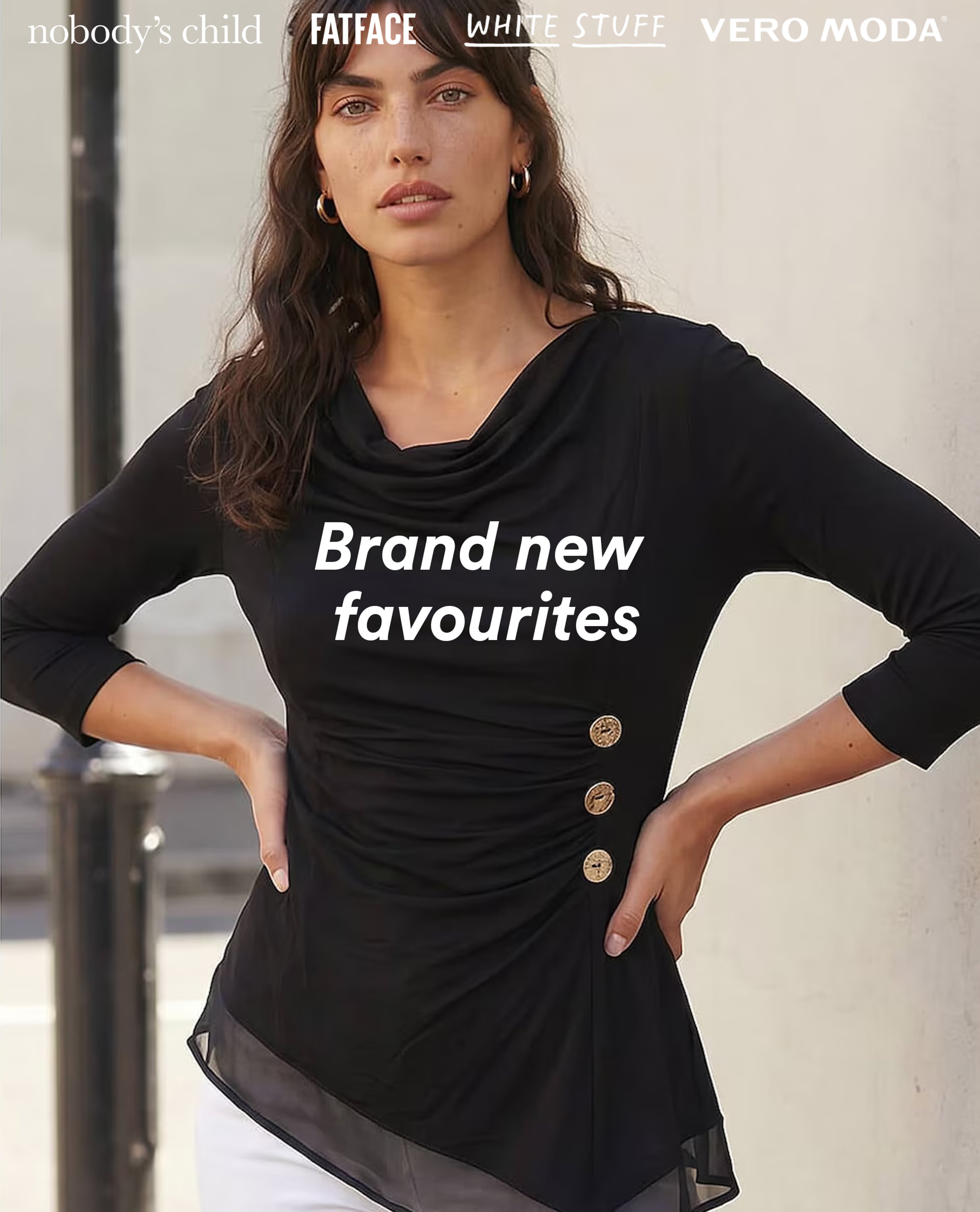 Woman wearing a black draped top with gold button details and white trousers.