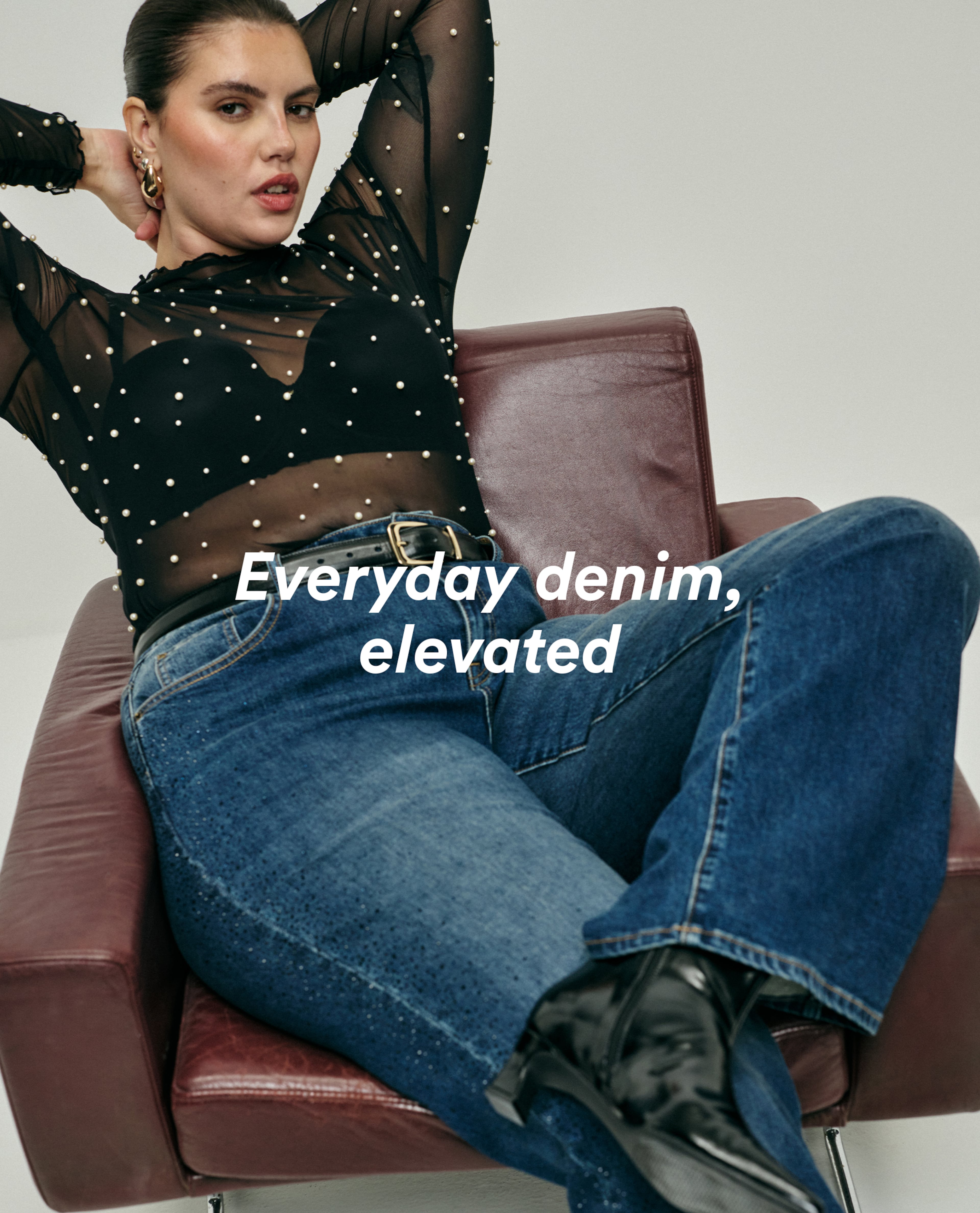 model wearing black xmas top and denim model sat on brown chair