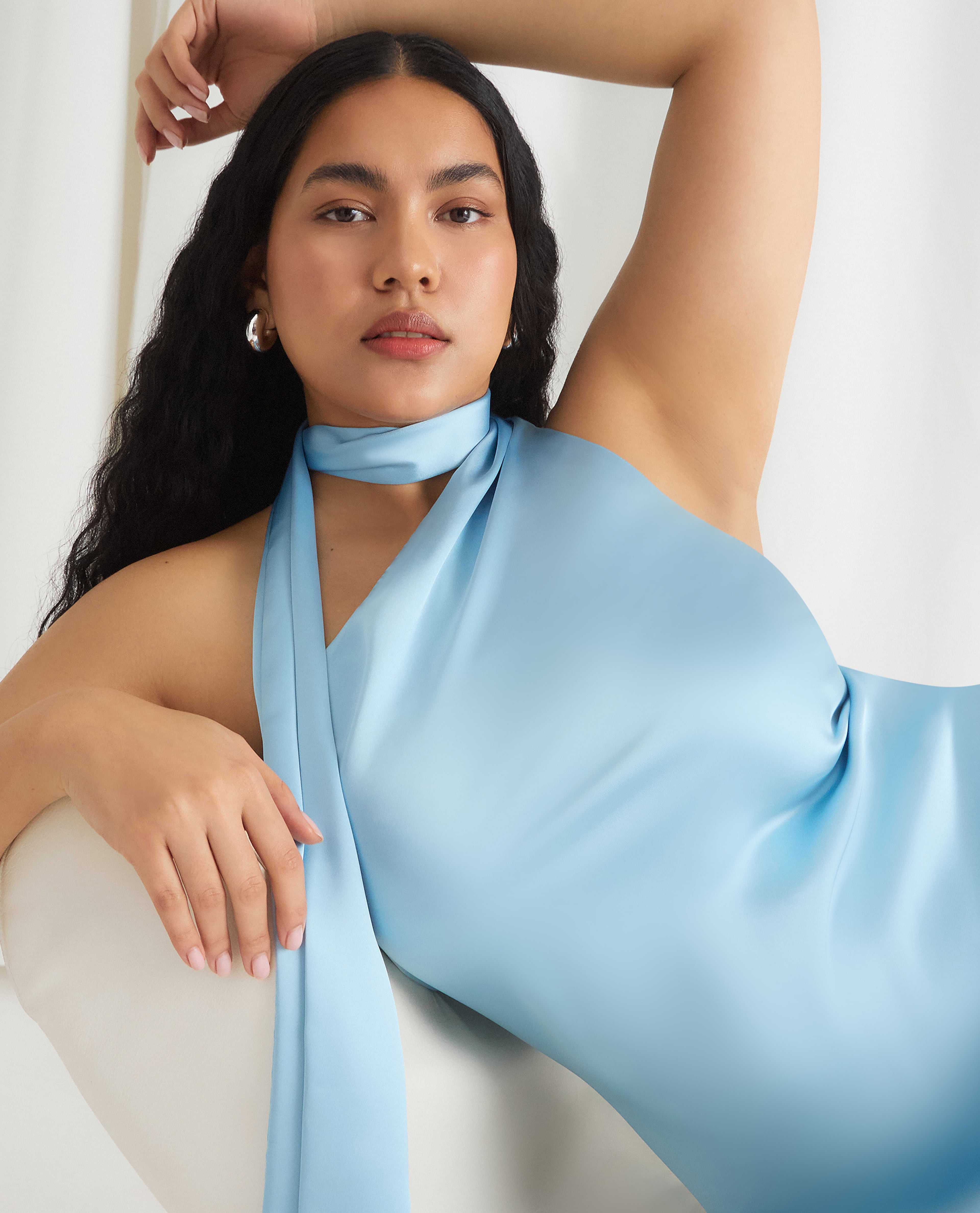 Model reclining in a light blue halter‑neck dress against a neutral indoor background.