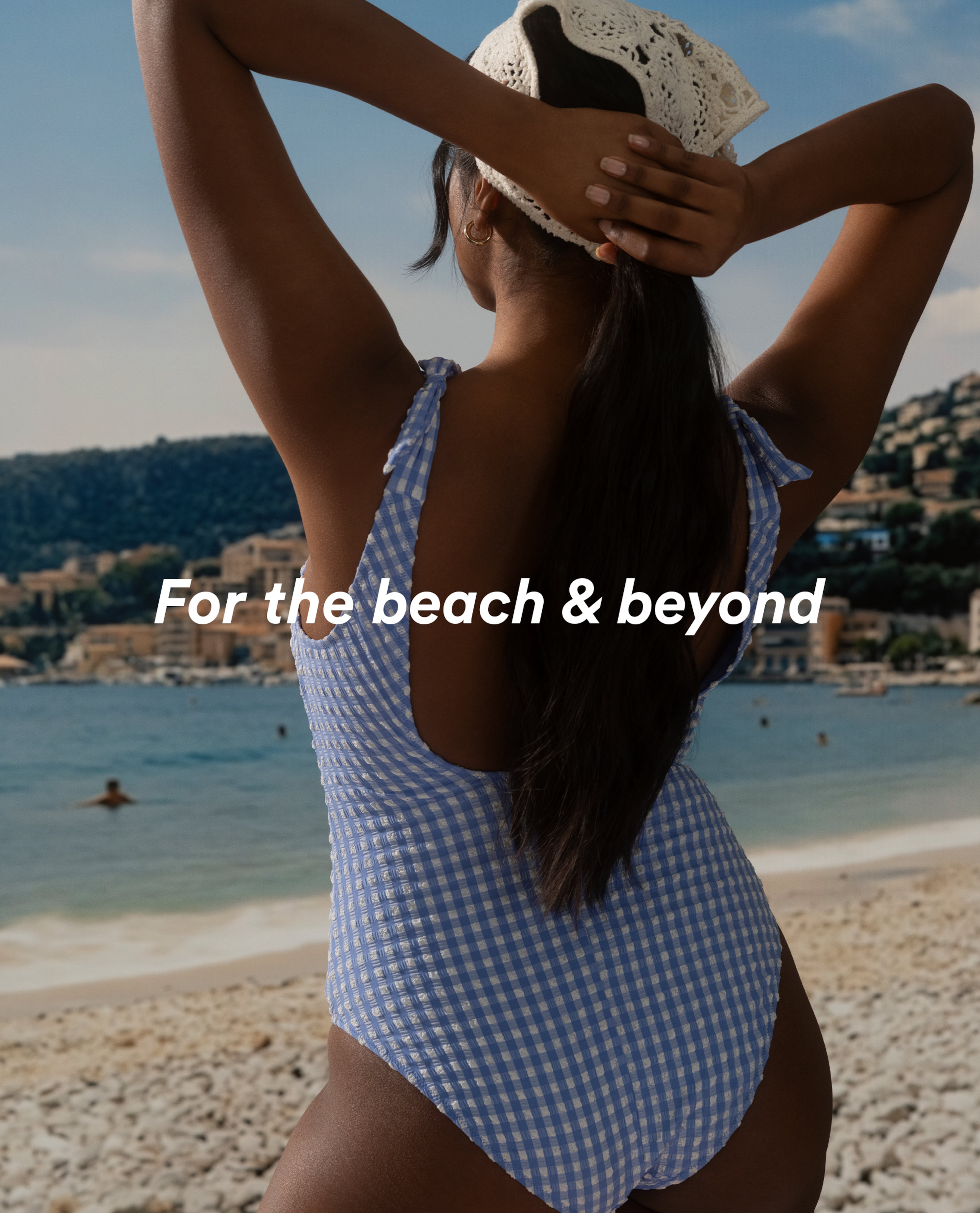 Person standing on a beach wearing a blue gingham swimsuit and sun hat.