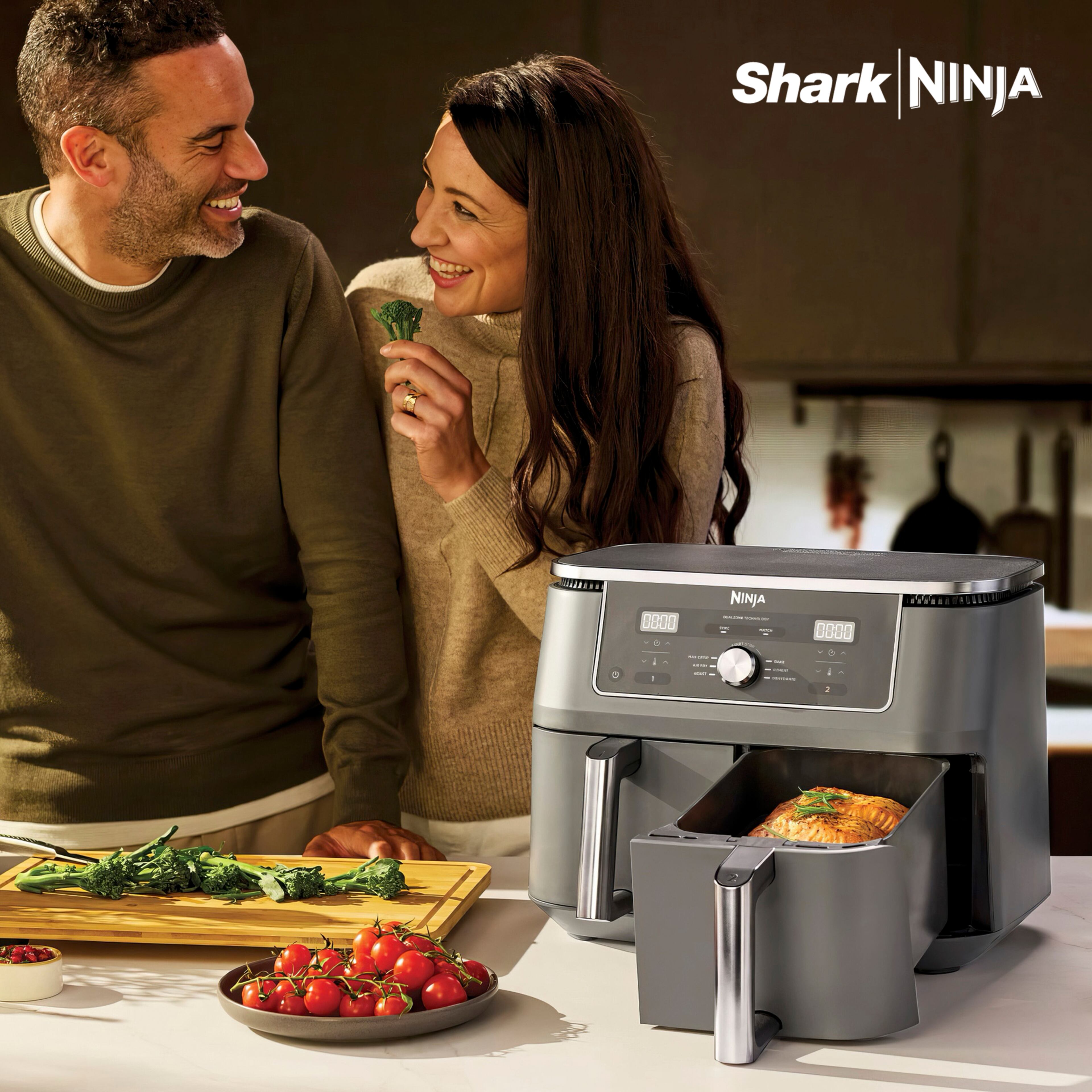 Shark Ninja
A man and woman preparing food together in a kitchen, with a Ninja dual-zone air fryer prominently displayed on the worktop. Fresh vegetables and a cooked salmon dish are shown alongside the appliance.