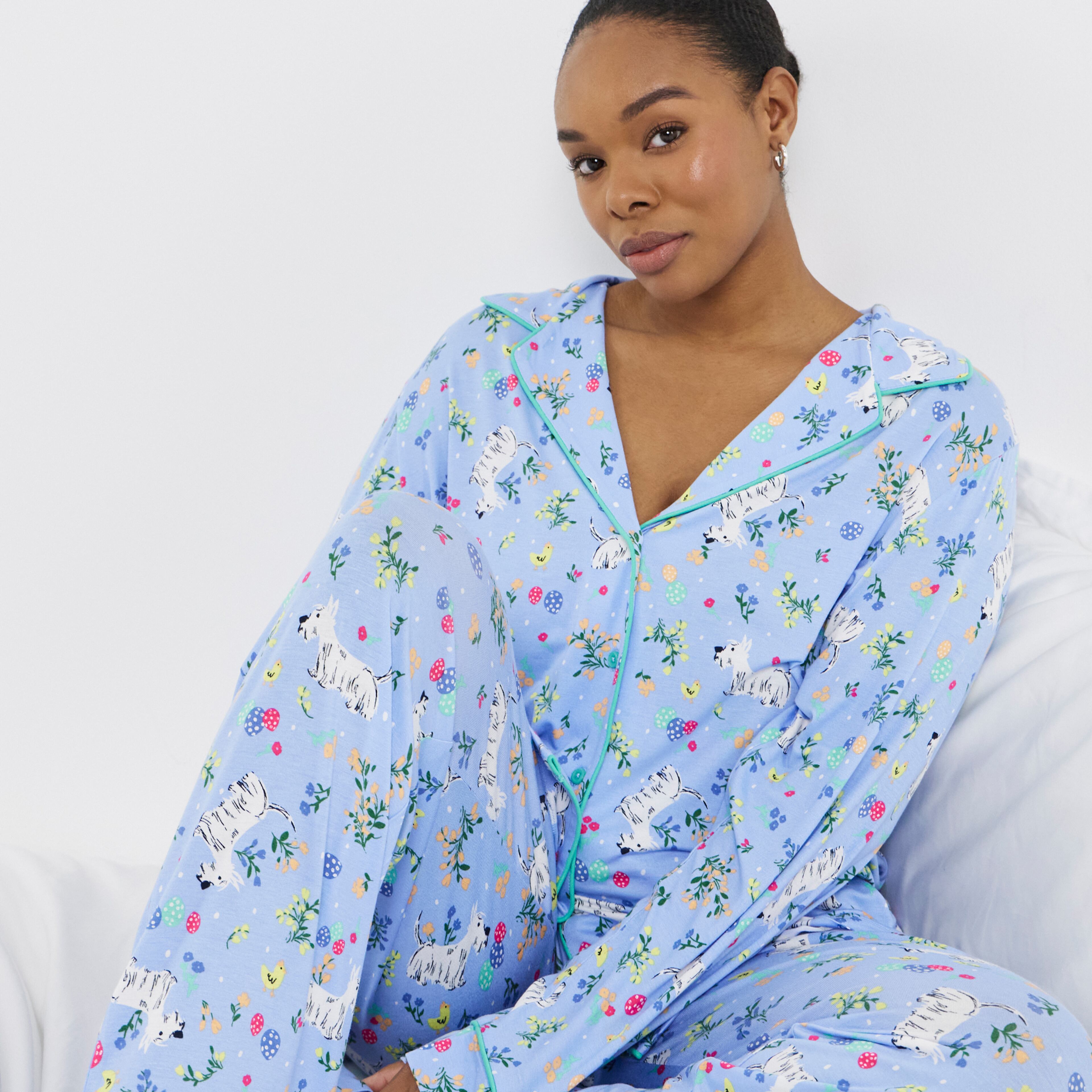 Person seated on white bedding wearing light blue printed pyjamas with animal and floral motifs.