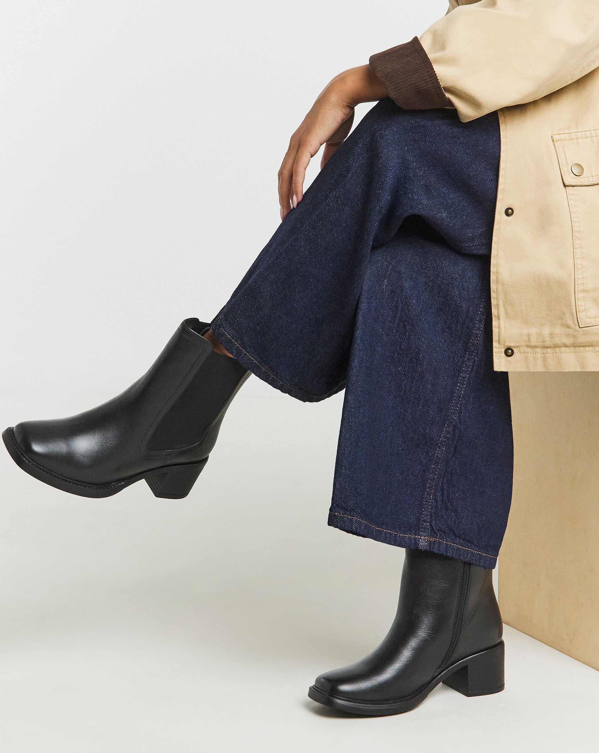 Black ankle boots paired with wide-leg dark denim jeans and a beige jacket.