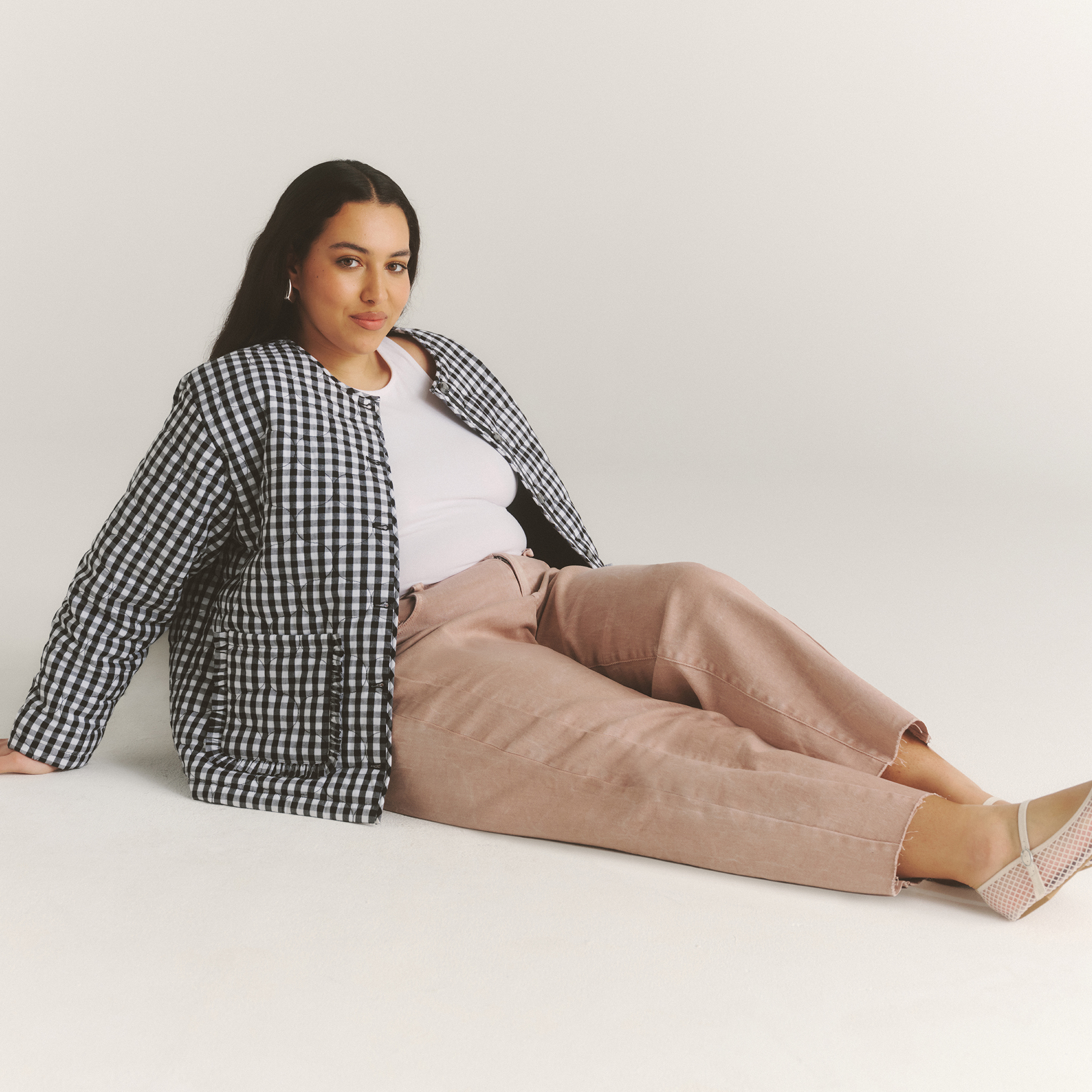 Model sat on floor wears cropped jeans and gingham jacket