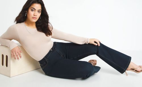 Model relaxing in nude coloured top and dark denim jeans