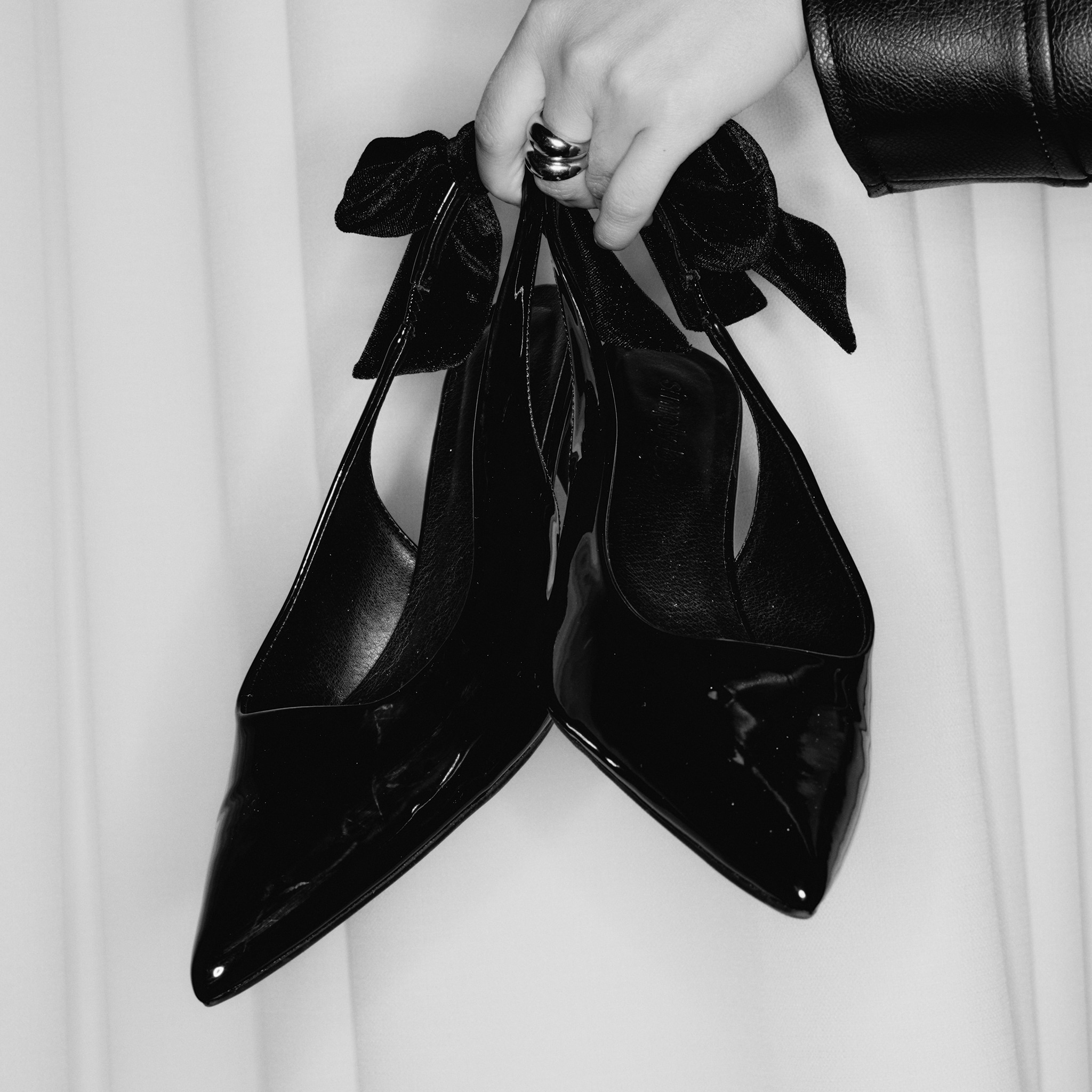 A pair of black court shoes with a bow on the back.