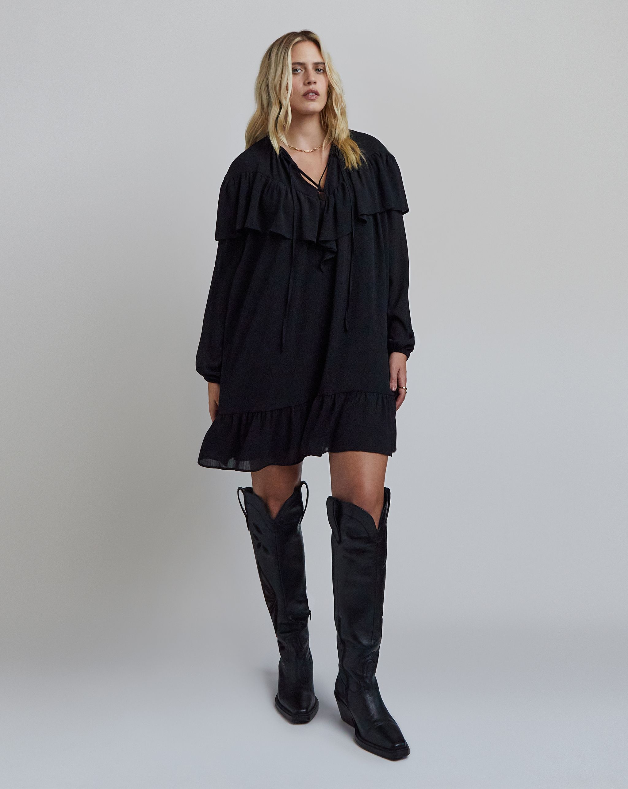 Model wears black dress and knee-high boots
