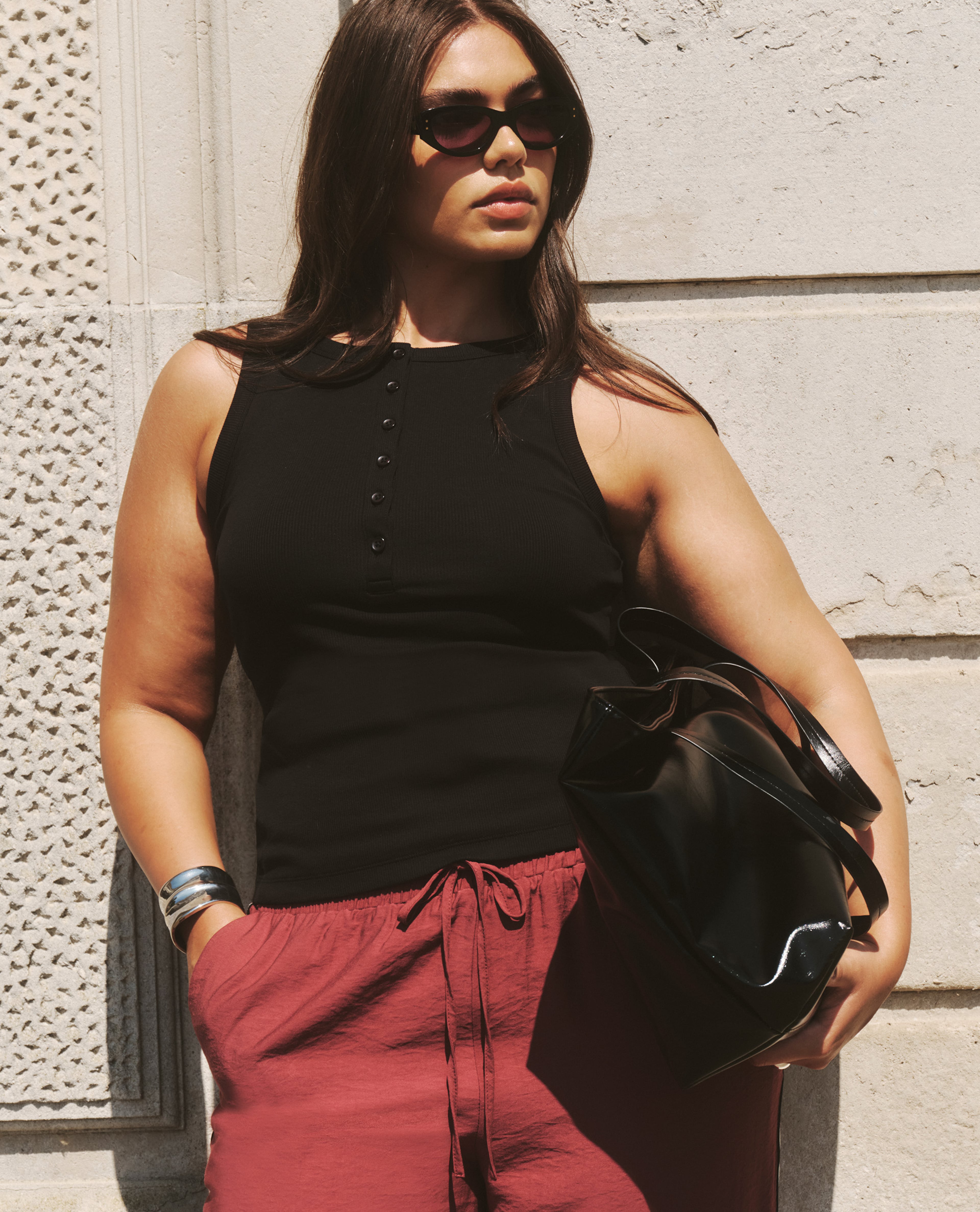 model wearing black top brown trousers holding bag at the side