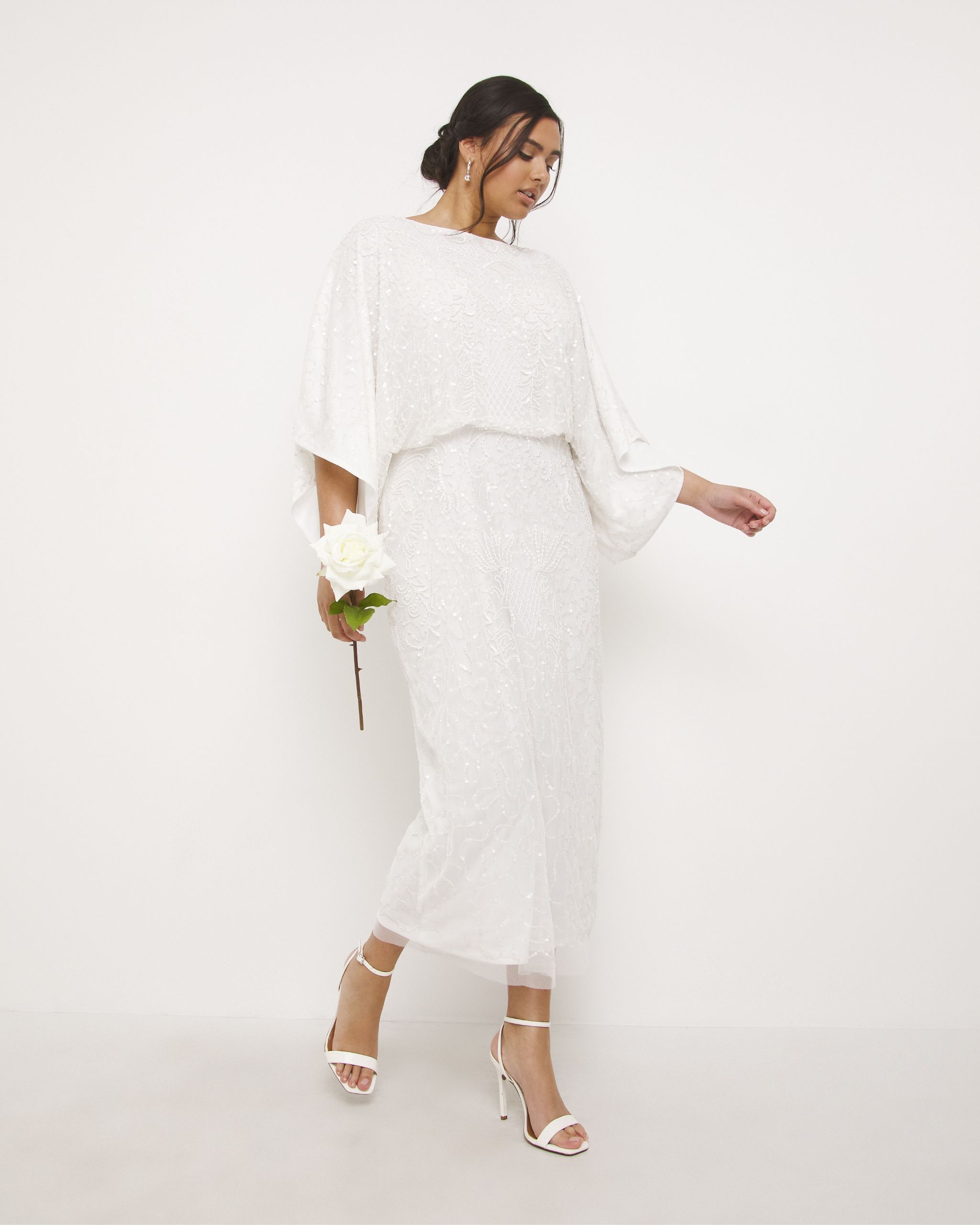 woman stood wearing a lacy waisted cream calf length dress.