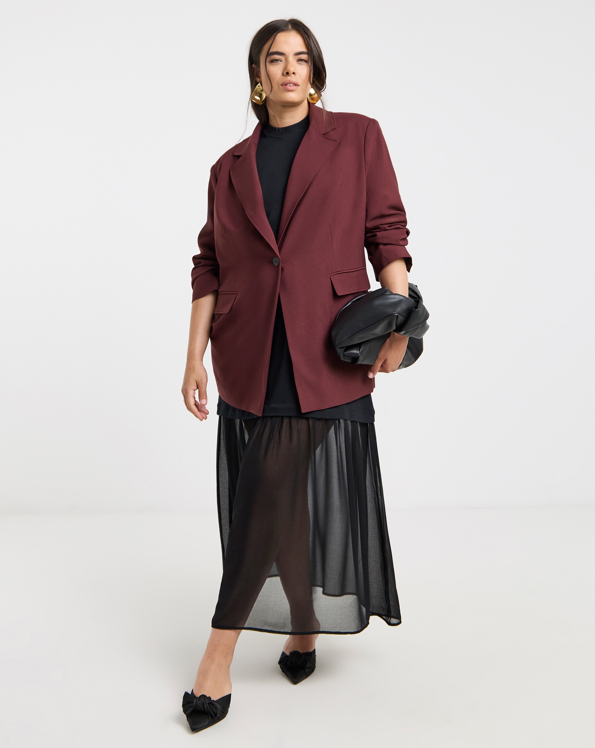 Model wears blazer in dark red over a black skirt and top