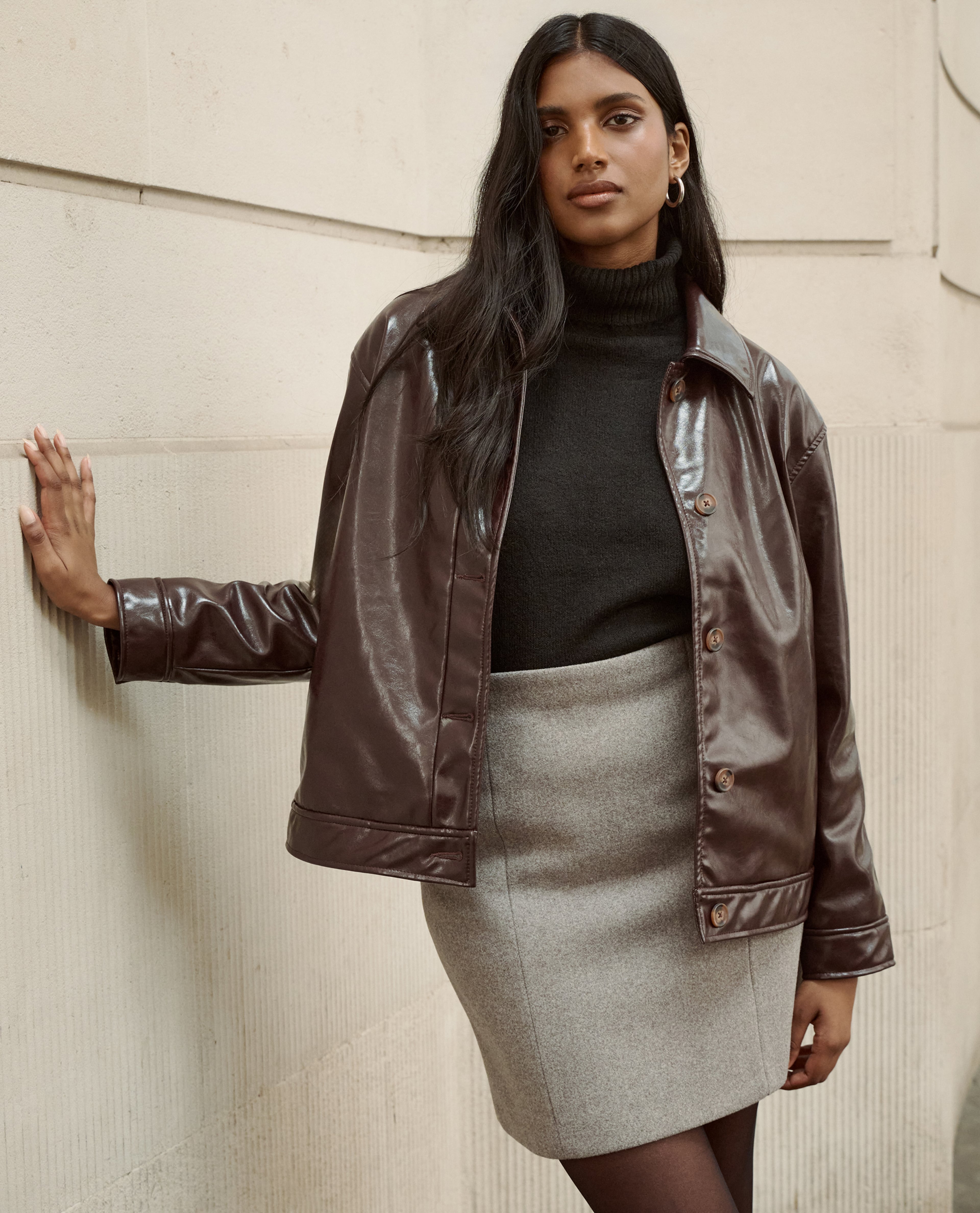Model wears leather jacket in chocolate and grey skirt