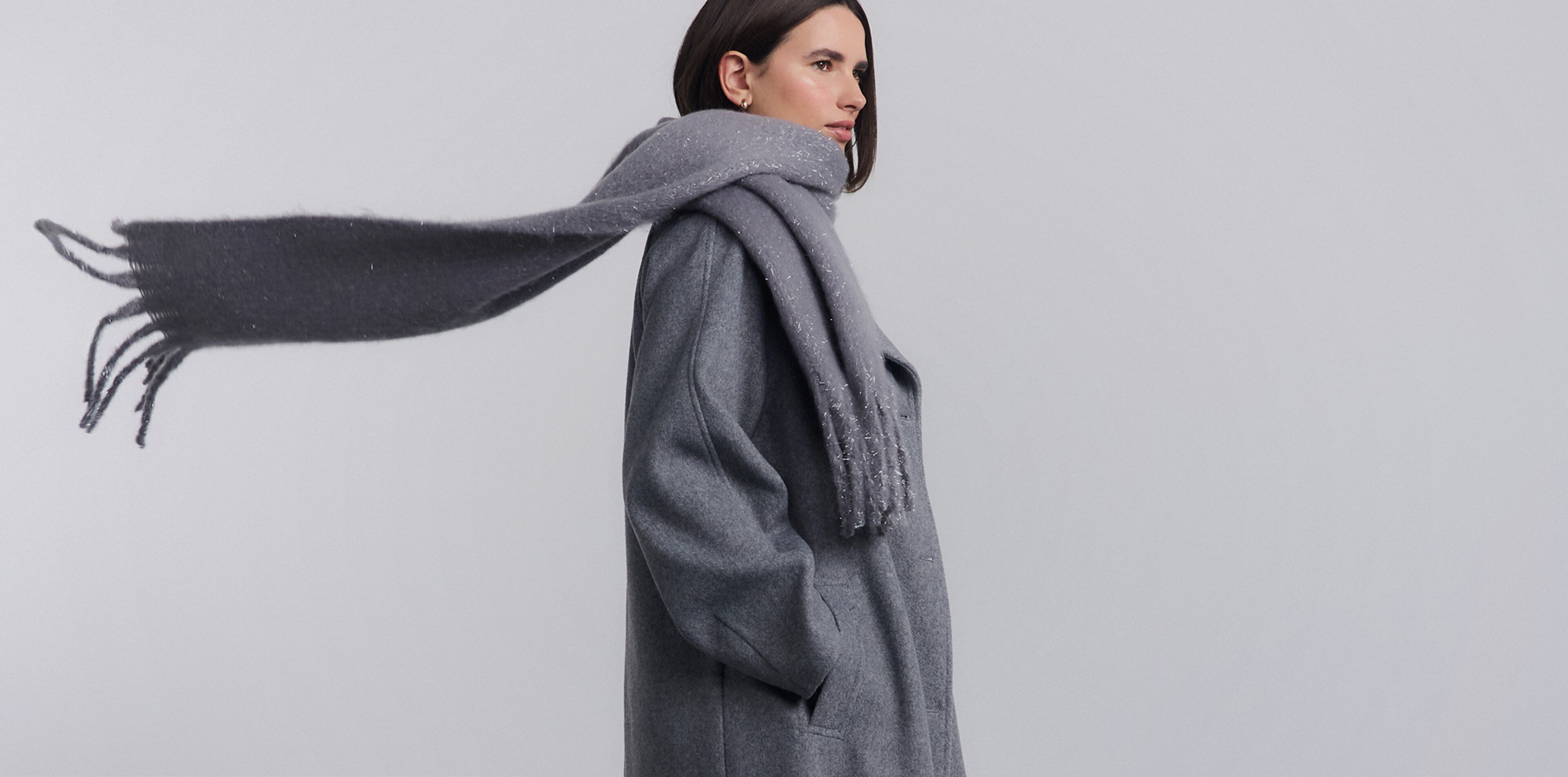Model wears grey overcoat with grey flowing scarf