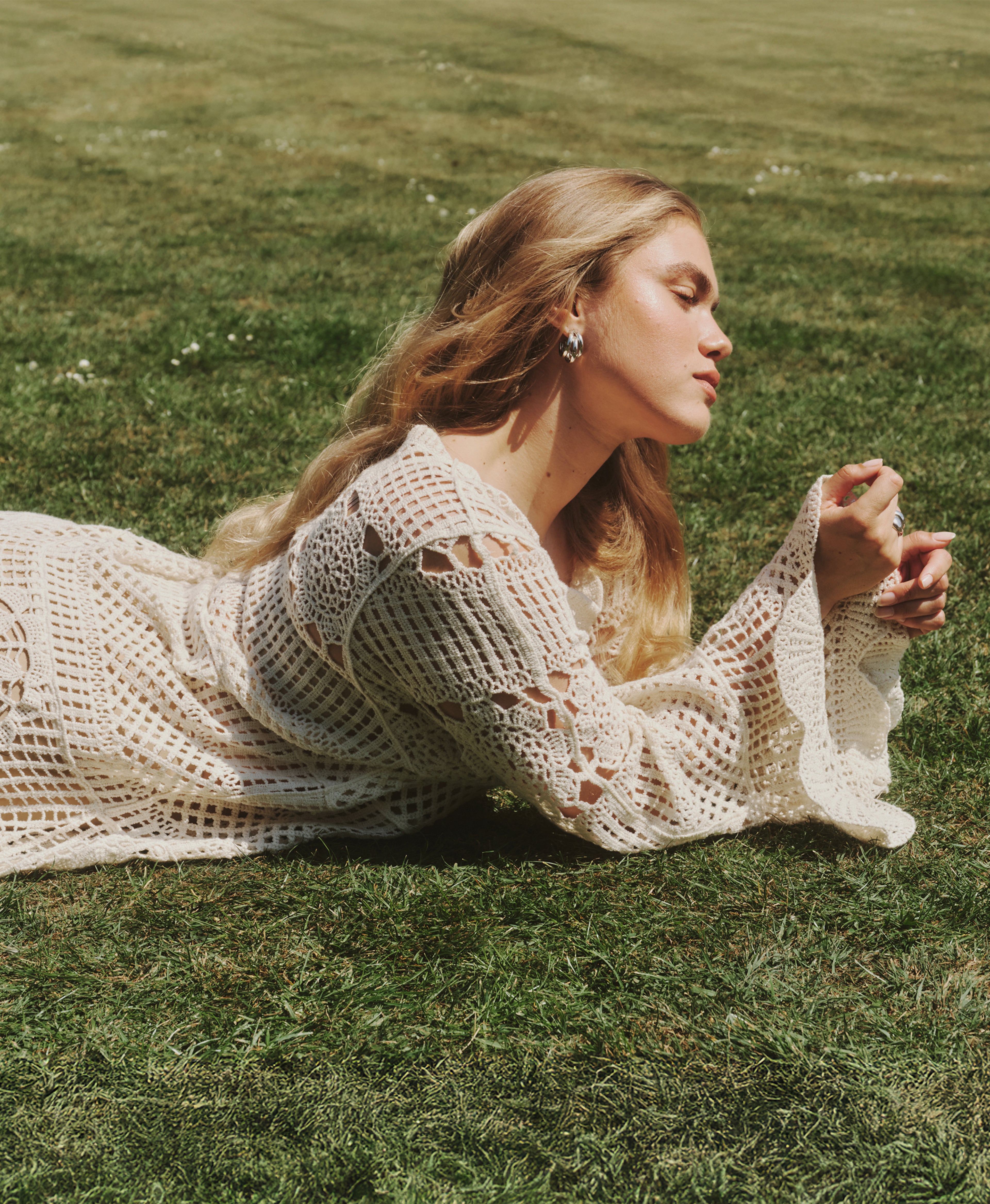 Model lay on grass wearing crochet dress