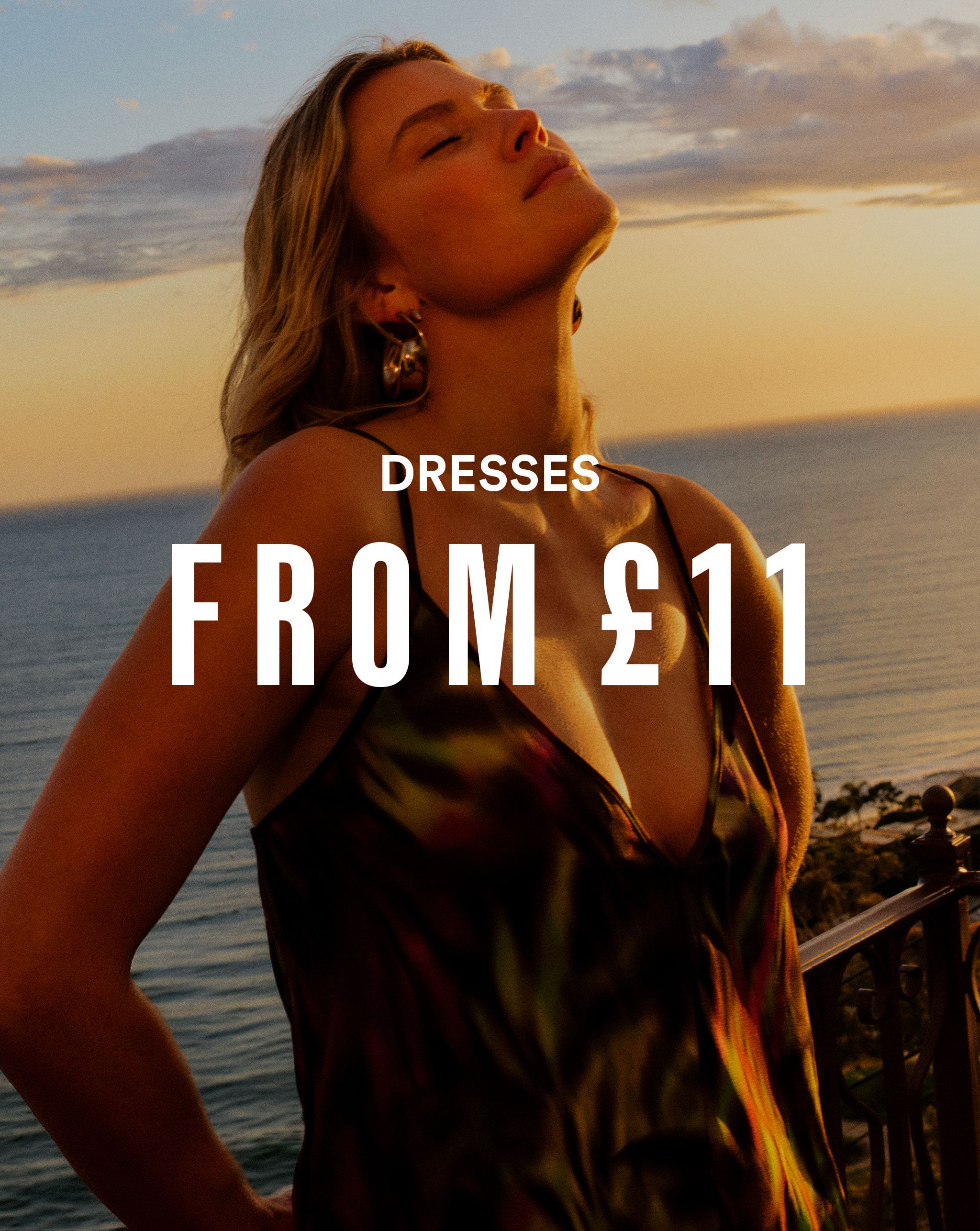 A woman stood by the sea wearing a low cut summer dress.