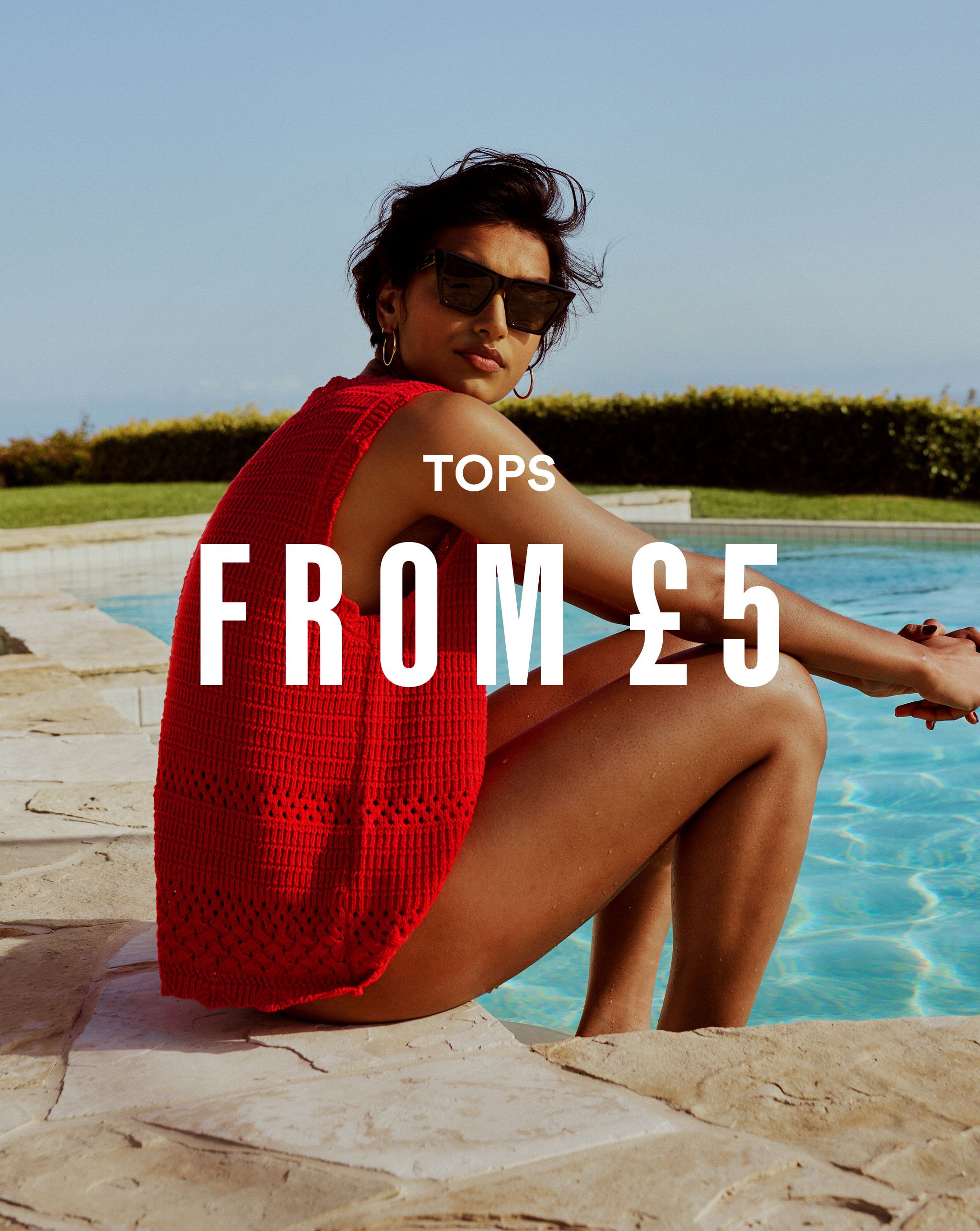 A model sat by a swimming pool wearing a red tanktop