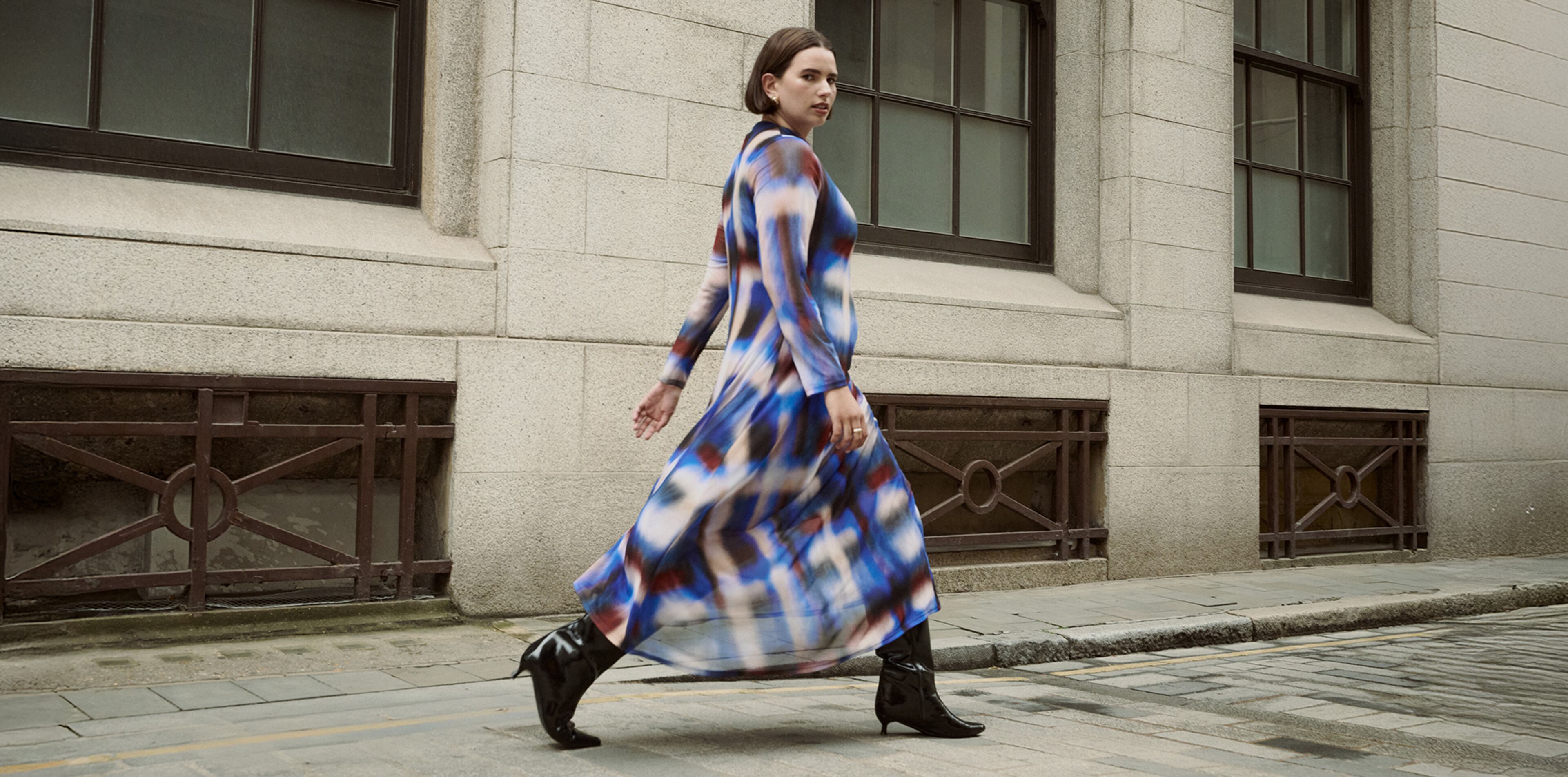 Model wears multi-coloured print dress and boots