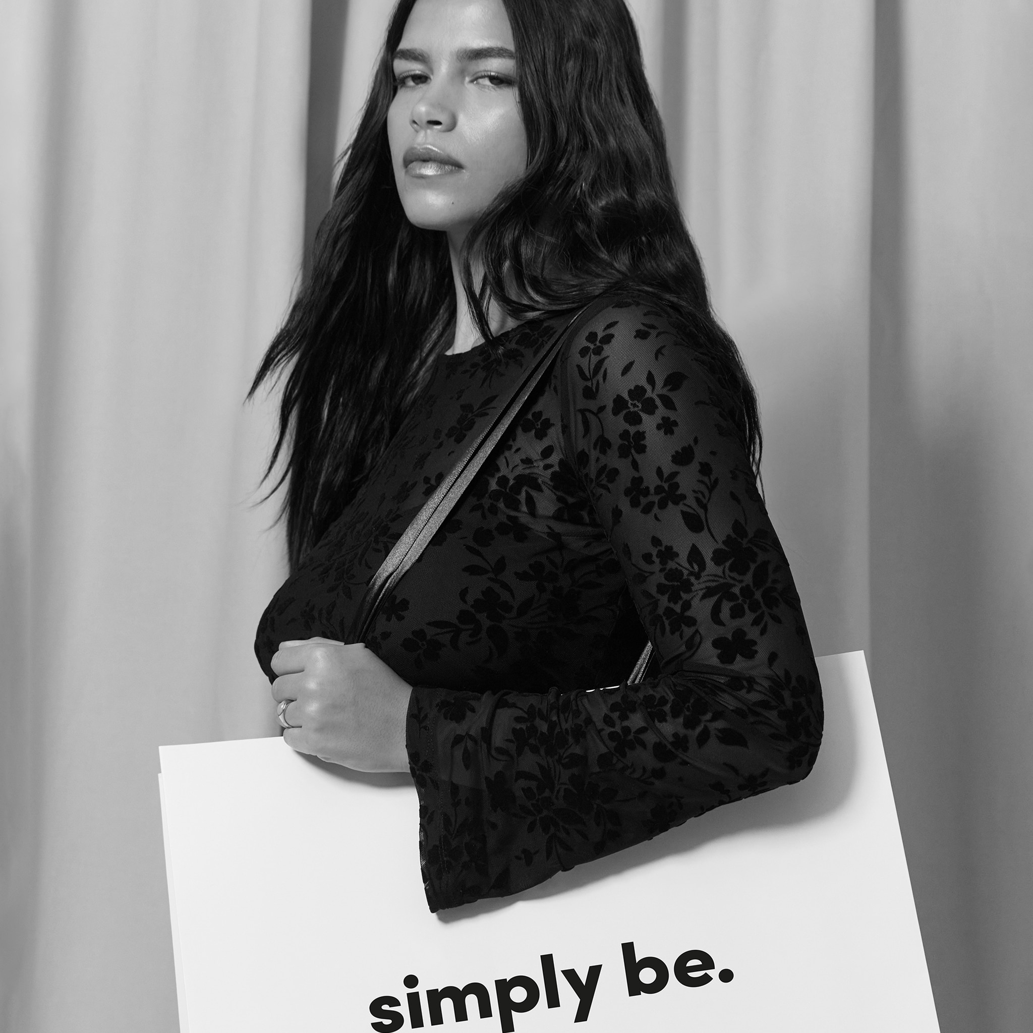 Model is wearing a long sleeve top, holding a white SimplyBe bag.