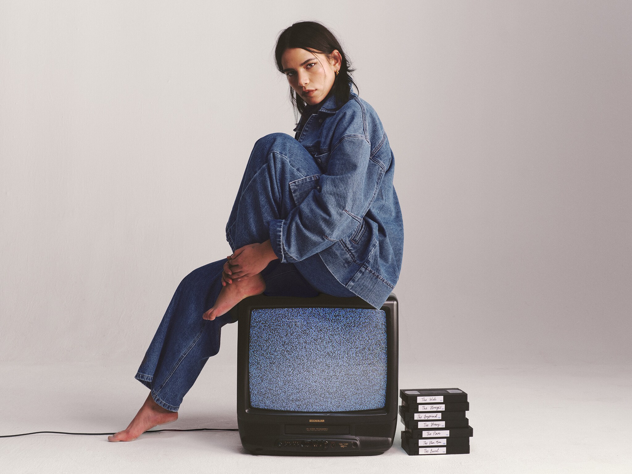 Model sat on old TV wears denim shirt and jeans