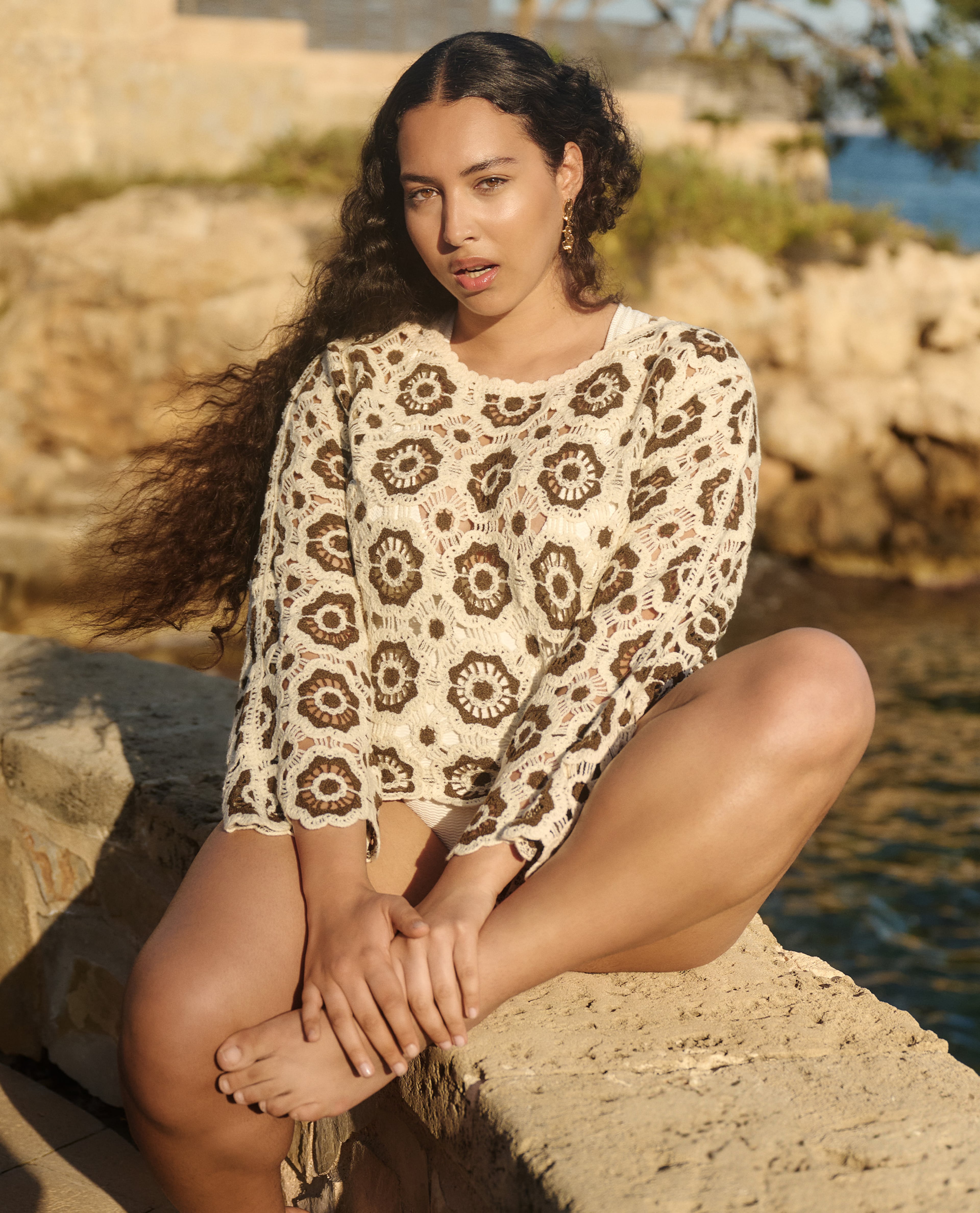 Model wearing cream and brown top. Sat on the rock.