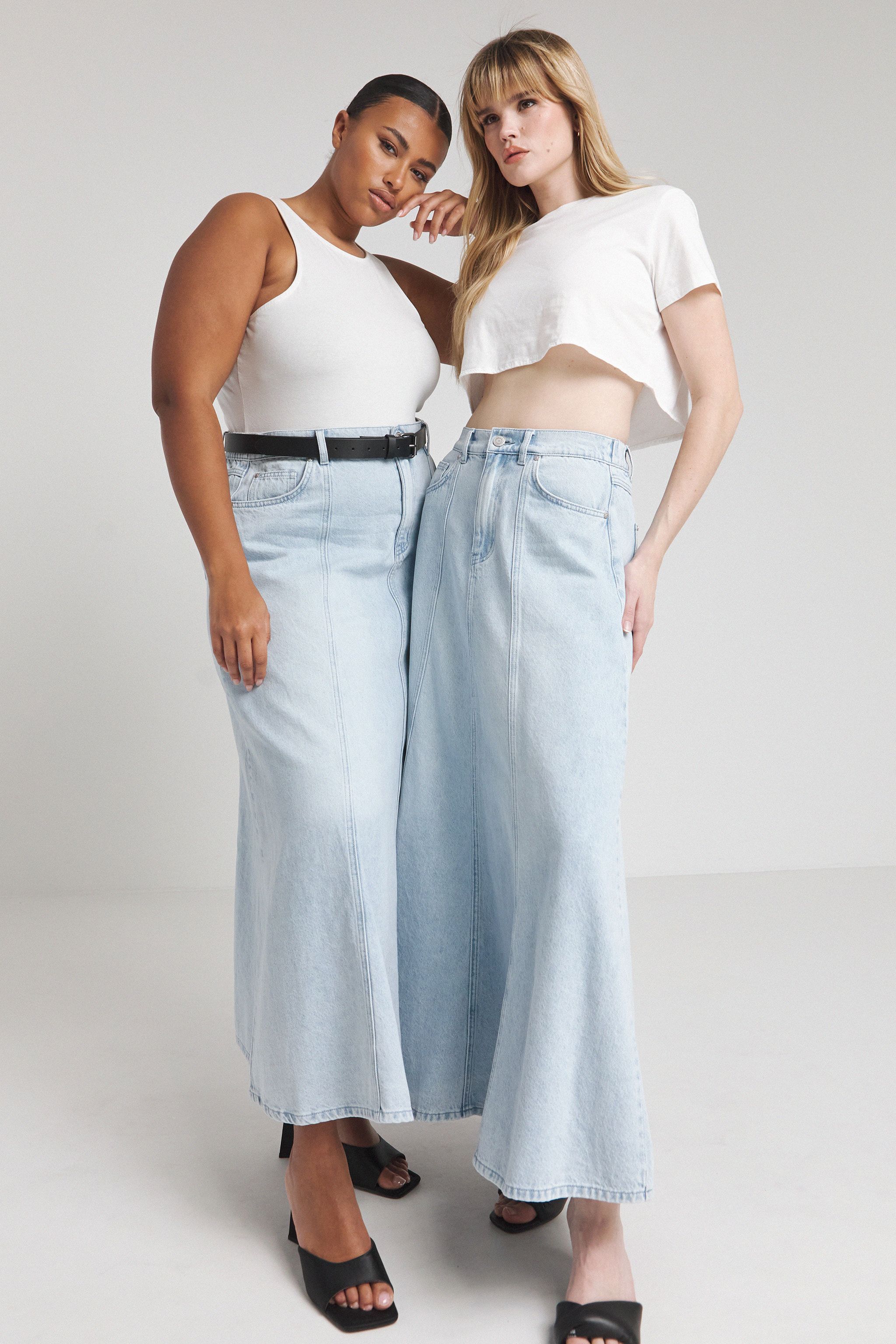Two models wear the denim maxi skirt with white tops