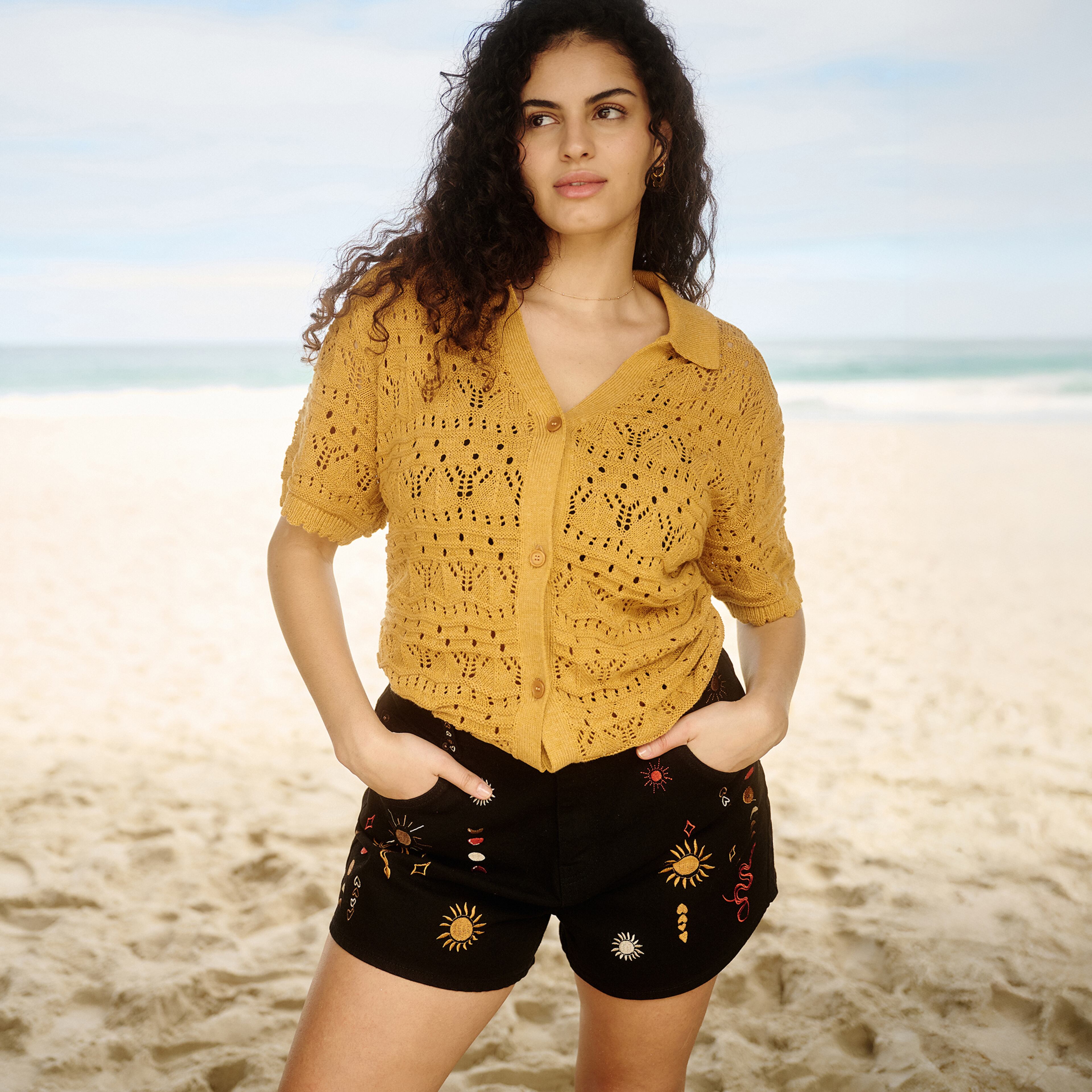 Model wears embroidered black shorts and crochet top