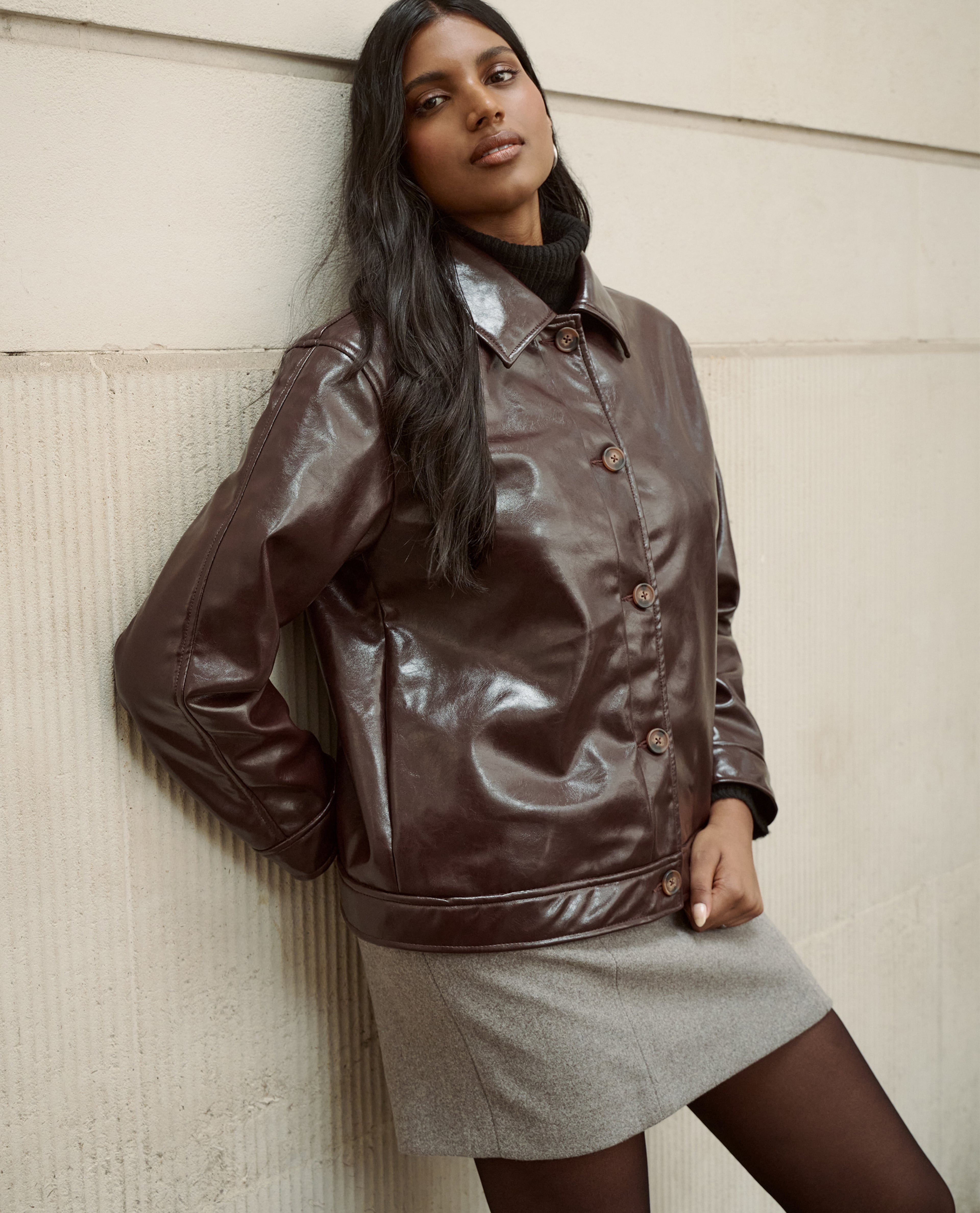 Model wears leather jacket in chocolate and skirt in grey